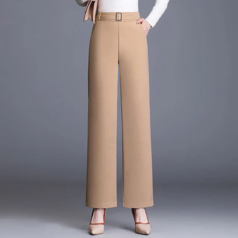 Woman wearing beige high-waisted wide-leg trousers with belt and beige heels on gray background
