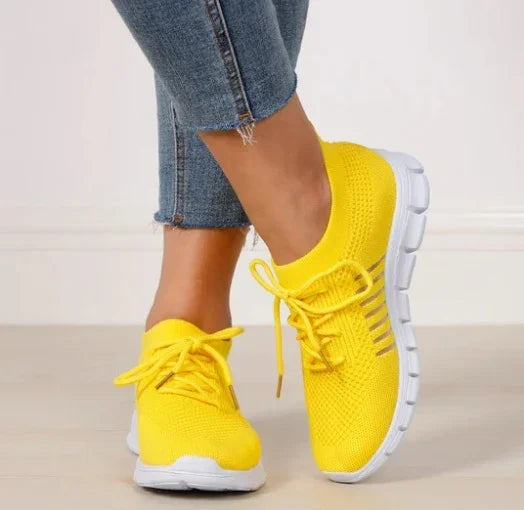 Person wearing bright yellow knit sneakers with white soles and blue jeans on a light floor