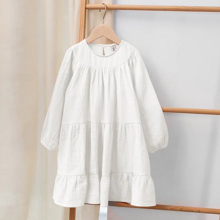 White long sleeve tiered baby dress hanging on wooden hanger against neutral background