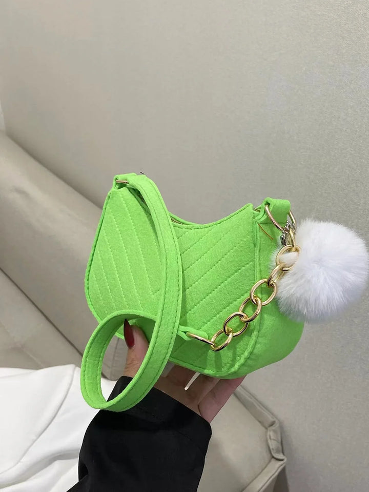 Bright green quilted handbag with gold chain and white fluffy pom-pom charm held indoors