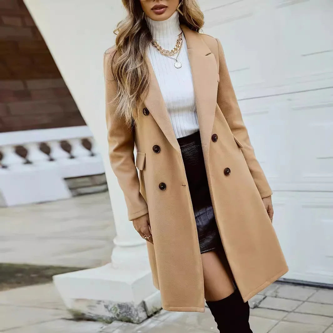 Woman wearing a camel double-breasted coat, white turtleneck sweater, black leather skirt, and gold chain necklaces