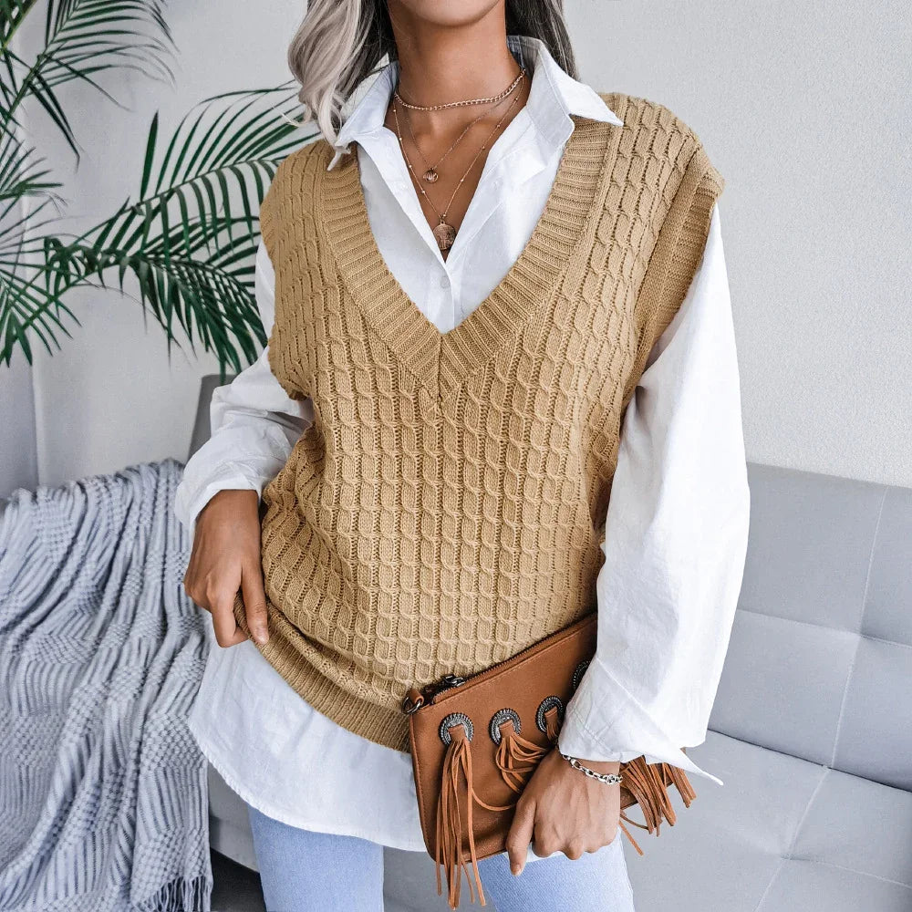 Woman wearing beige knitted vest over white shirt holding brown fringed clutch in modern living room