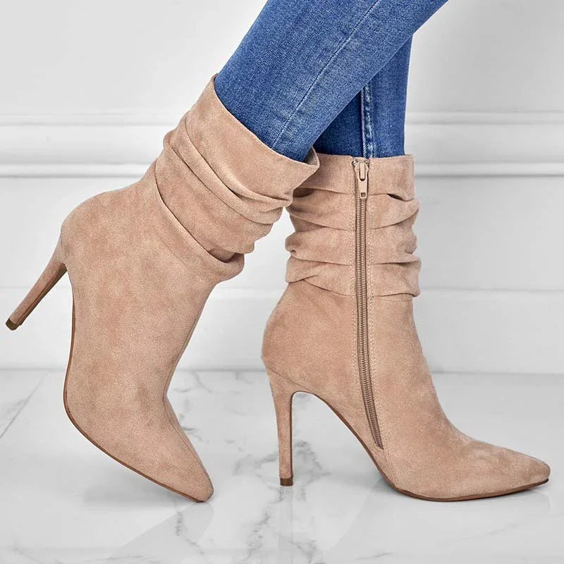 Beige suede high-heeled slouchy ankle boots worn with blue skinny jeans on marble floor