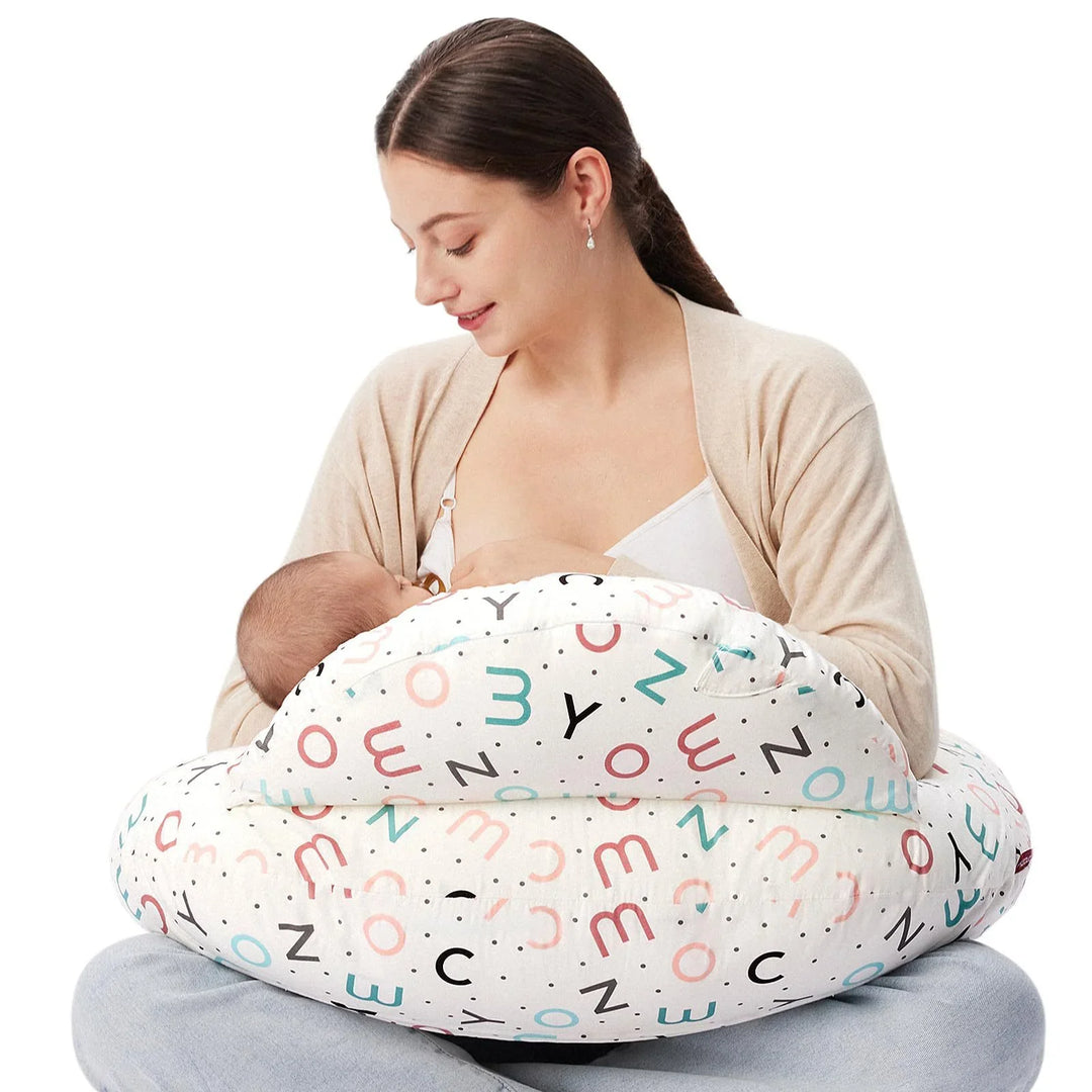 Mother breastfeeding baby seated with alphabet print nursing pillow on white background
