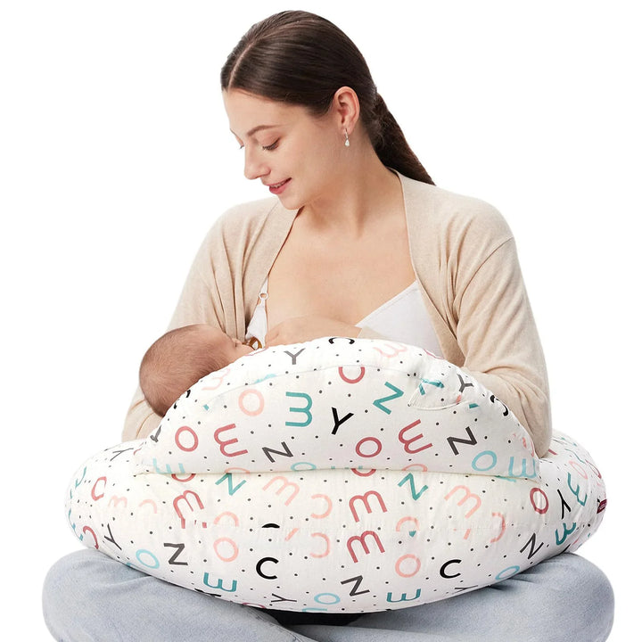 Mother breastfeeding baby seated with alphabet print nursing pillow on white background