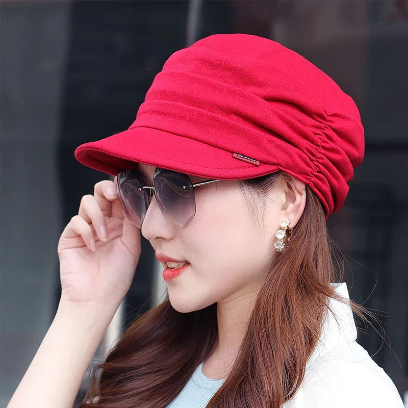 Woman wearing a bright red newsboy cap and stylish sunglasses with gold earrings