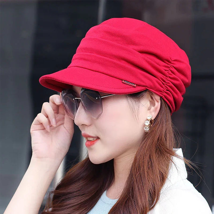 Woman wearing a bright red newsboy cap and stylish sunglasses with gold earrings