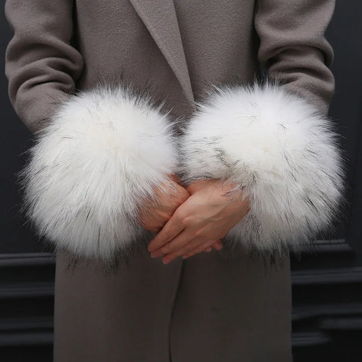 Woman wearing brown coat with large white fur cuffs on sleeves, hands clasped