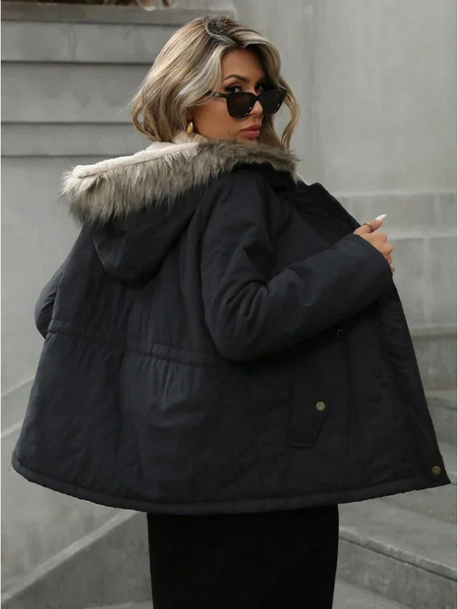 Stylish woman wearing black winter jacket with fur-trimmed hood and sunglasses on urban stairs