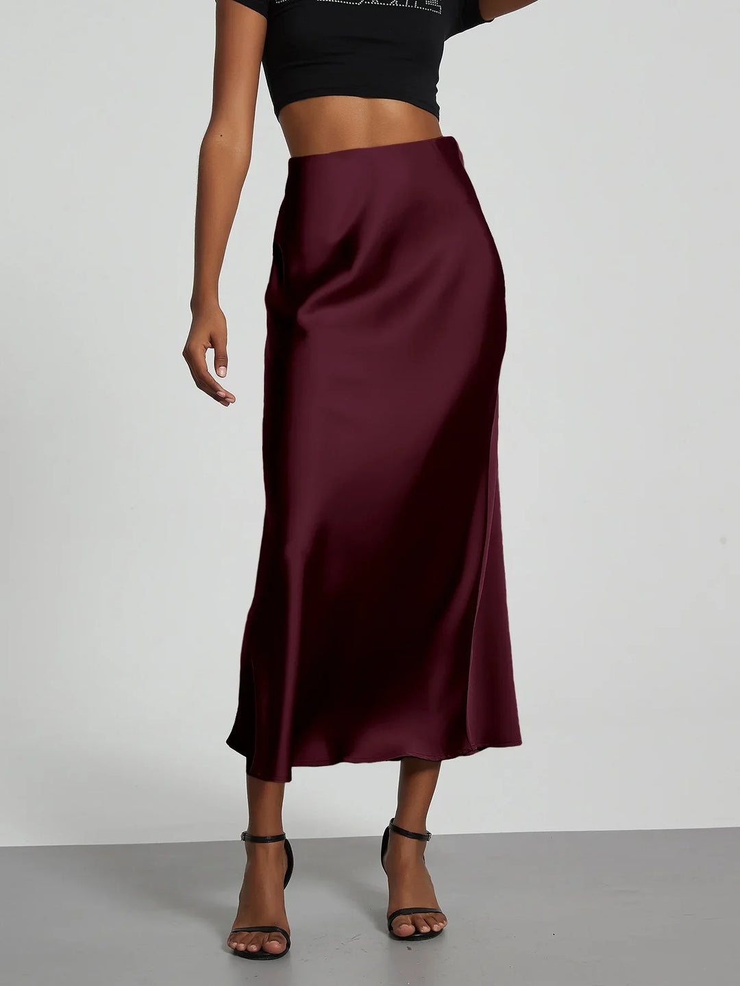 Woman wearing a burgundy satin midi skirt with a black crop top and black ankle-strap heels