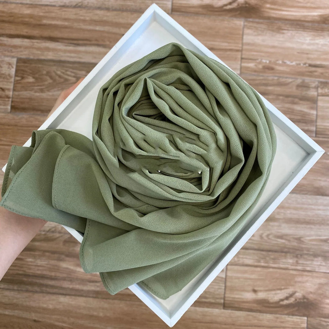 Hand holding a white square tray with a neatly folded olive green fabric cloth on wooden floor