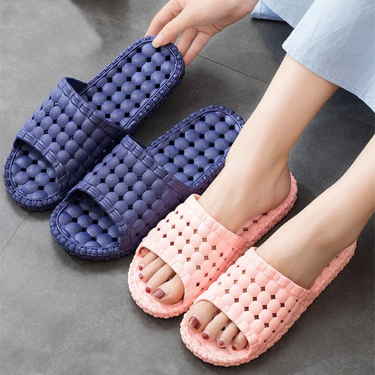Pair of blue and pink open-toe slippers with bubble texture, worn by a person on grey floor