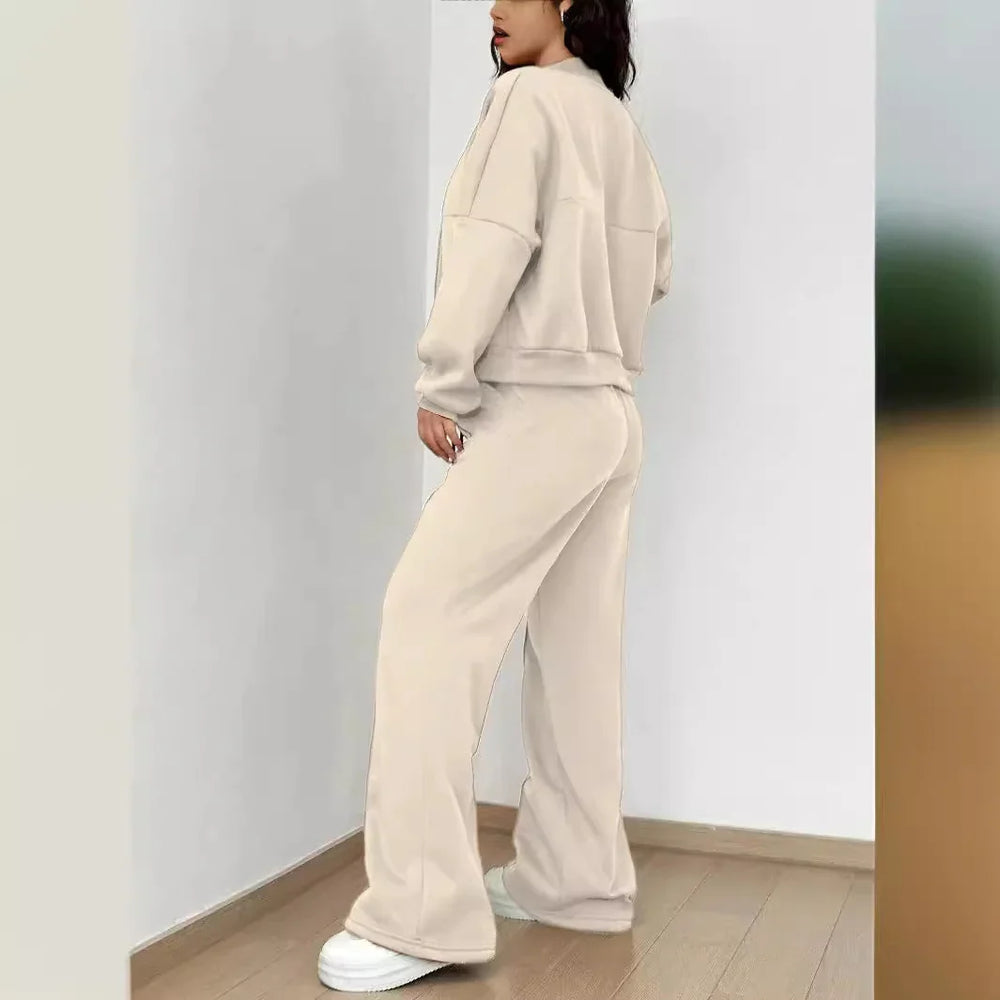 Woman in beige oversized sweatshirt and wide-leg pants with white sneakers standing indoors