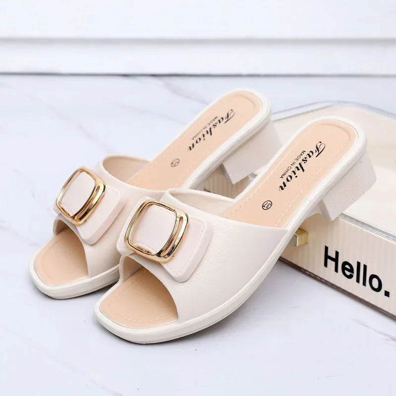 Pair of white open-toe block heel women’s sandals with gold buckle detail on marble surface