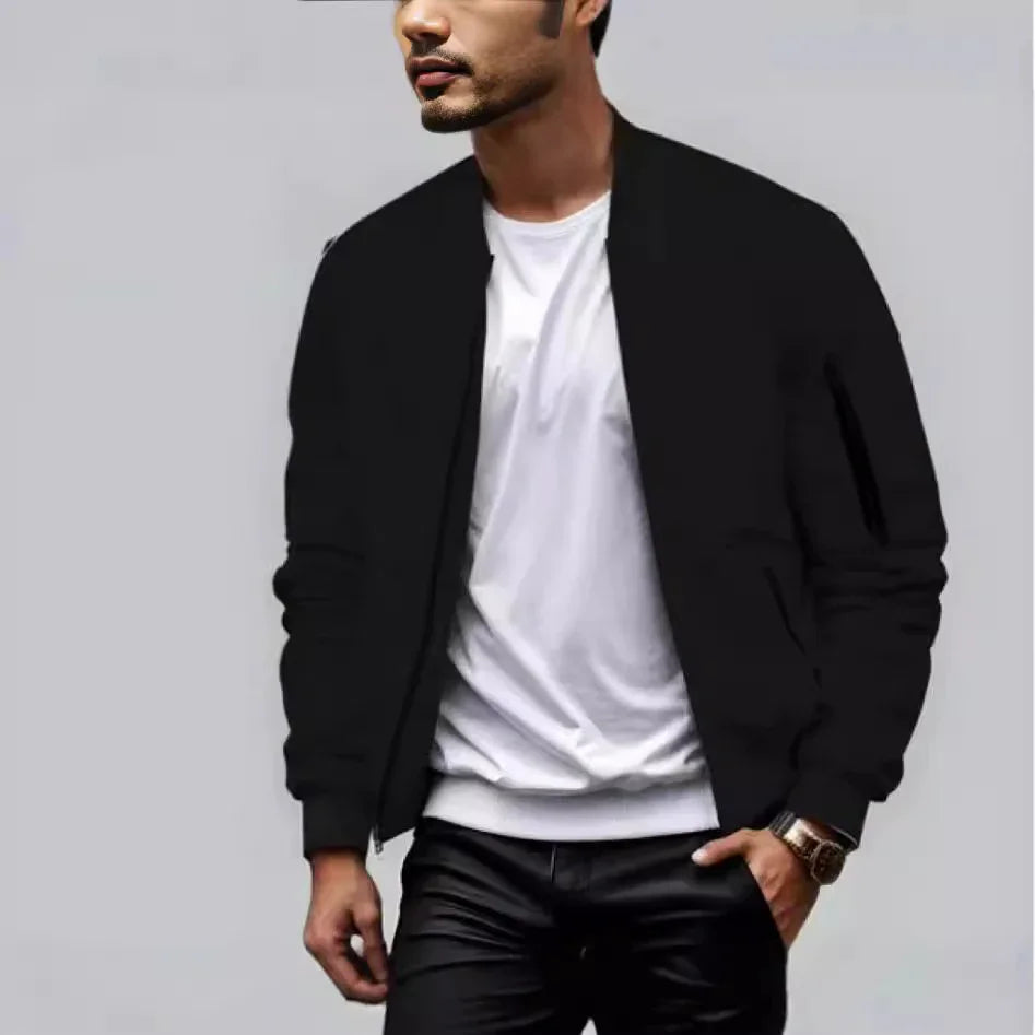 Man wearing black bomber jacket, white t-shirt, black pants, and wristwatch against gray background
