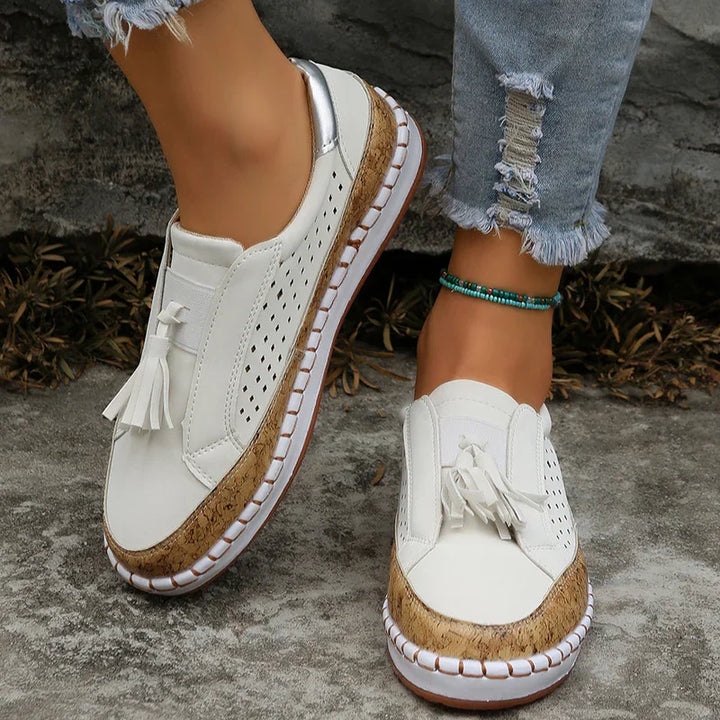 White slip-on casual shoes with tassels, cork sole, and perforated sides worn with distressed jeans and turquoise anklet