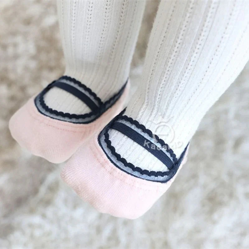 Close-up of baby feet wearing white knit tights with pink and navy Mary Jane style velvet booties
