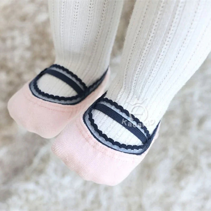Close-up of baby feet wearing white knit tights with pink and navy Mary Jane style velvet booties
