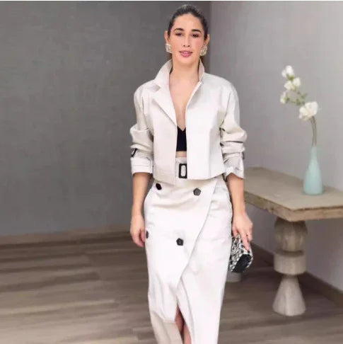 Woman in stylish cream cropped jacket and high-waist buttoned skirt holding small clutch indoors