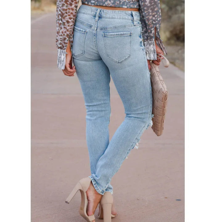 Woman wearing light blue distressed skinny jeans, beige high heels, and animal print top holding woven beige clutch bag