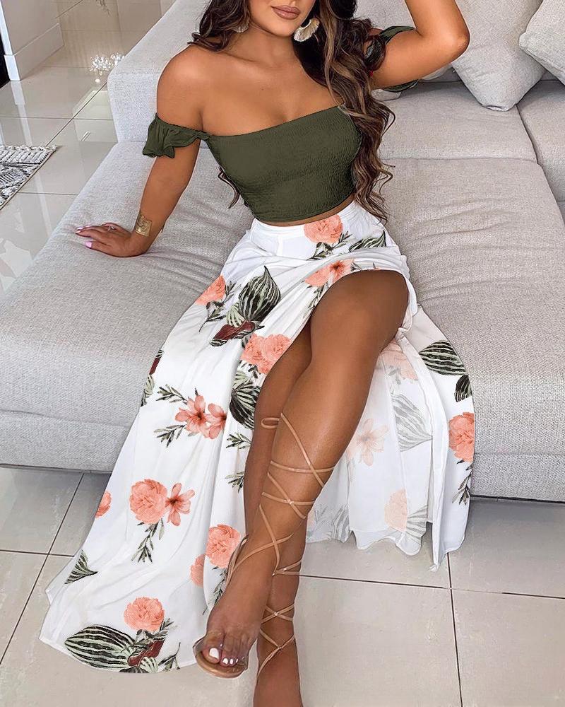 Woman sitting on a gray sofa wearing an olive green off-shoulder top and white floral high-slit skirt with lace-up sandals