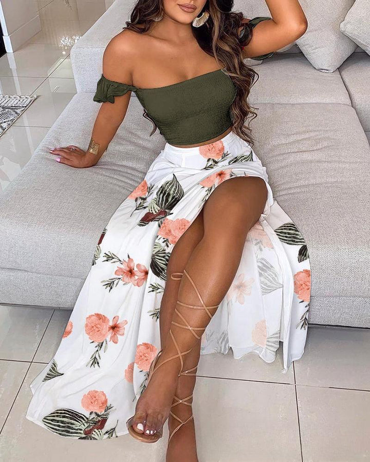 Woman sitting on a gray sofa wearing an olive green off-shoulder top and white floral high-slit skirt with lace-up sandals