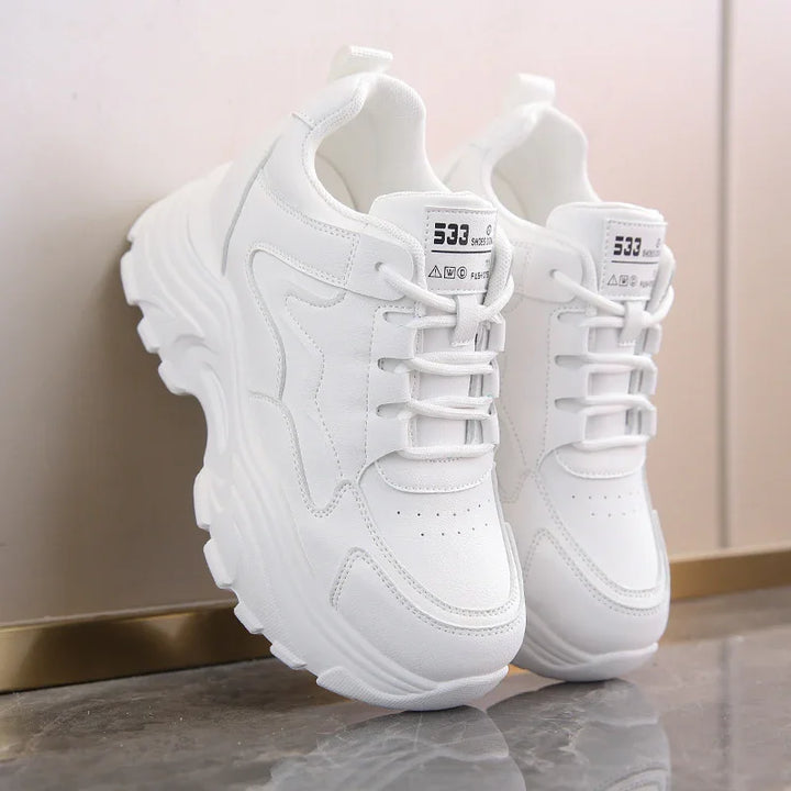 Pair of white chunky sneakers with thick soles and lace-up design on glossy surface