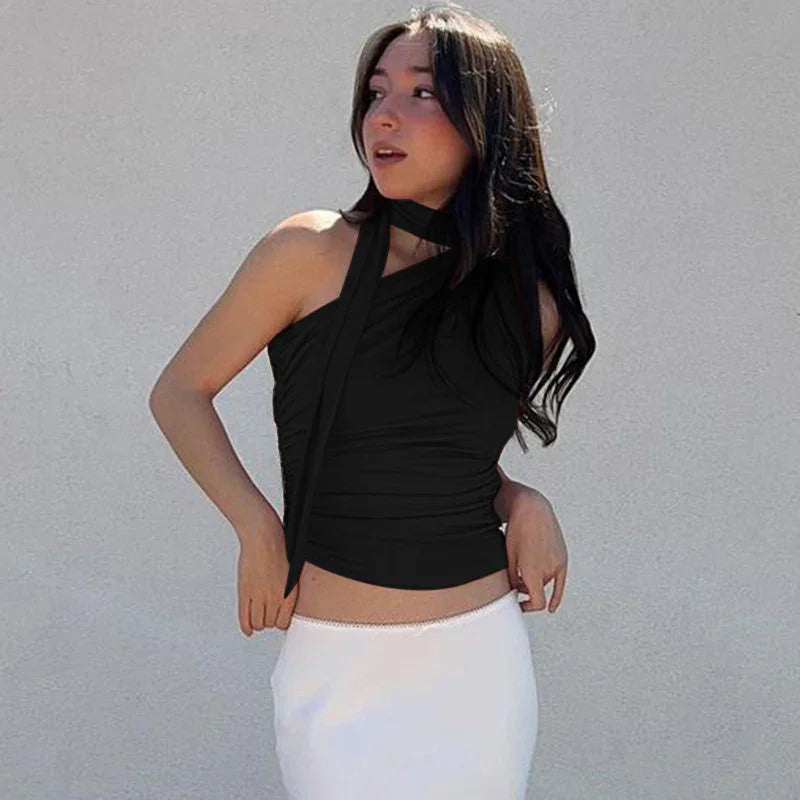Woman wearing black sleeveless top with scarf detail and white skirt against gray wall