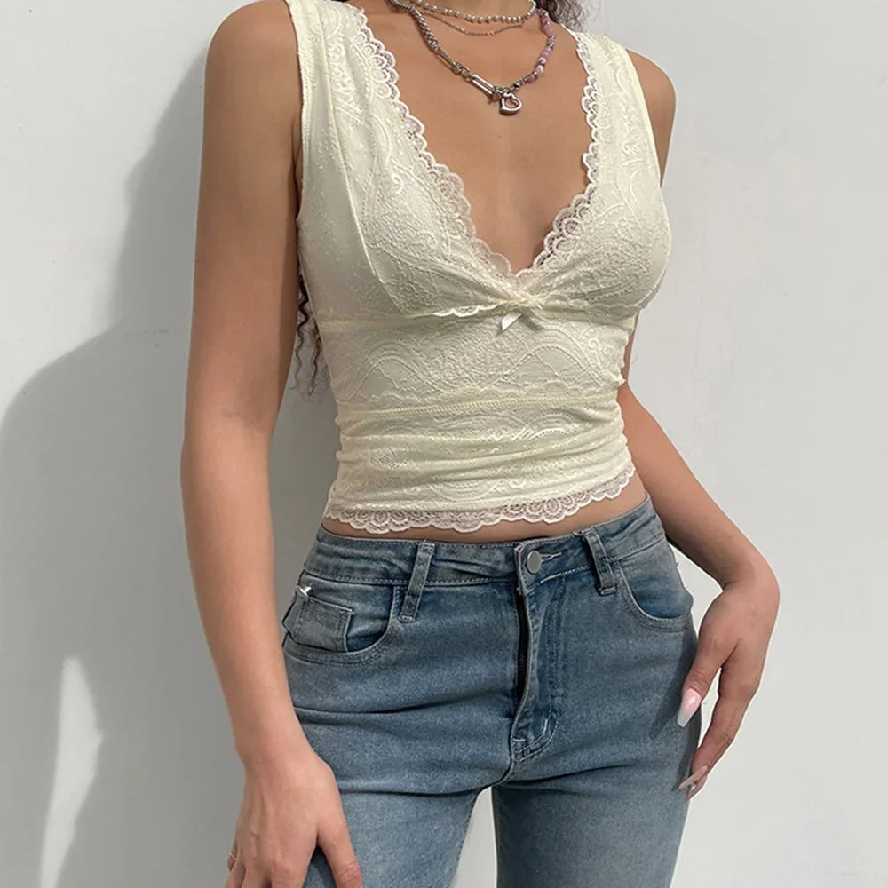 woman wearing cream lace sleeveless crop top paired with high waist blue jeans against white background