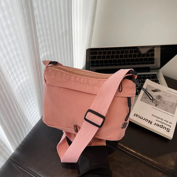 pink crossbody bag with adjustable strap held in hand near laptop and book on black surface
