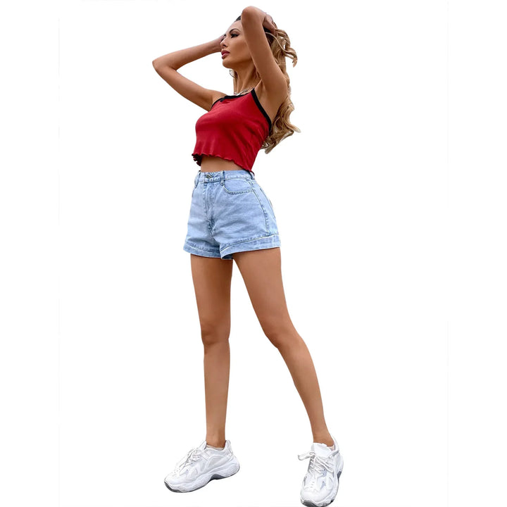 Woman in red cropped tank top, light blue high-waisted denim shorts, and white sneakers posing
