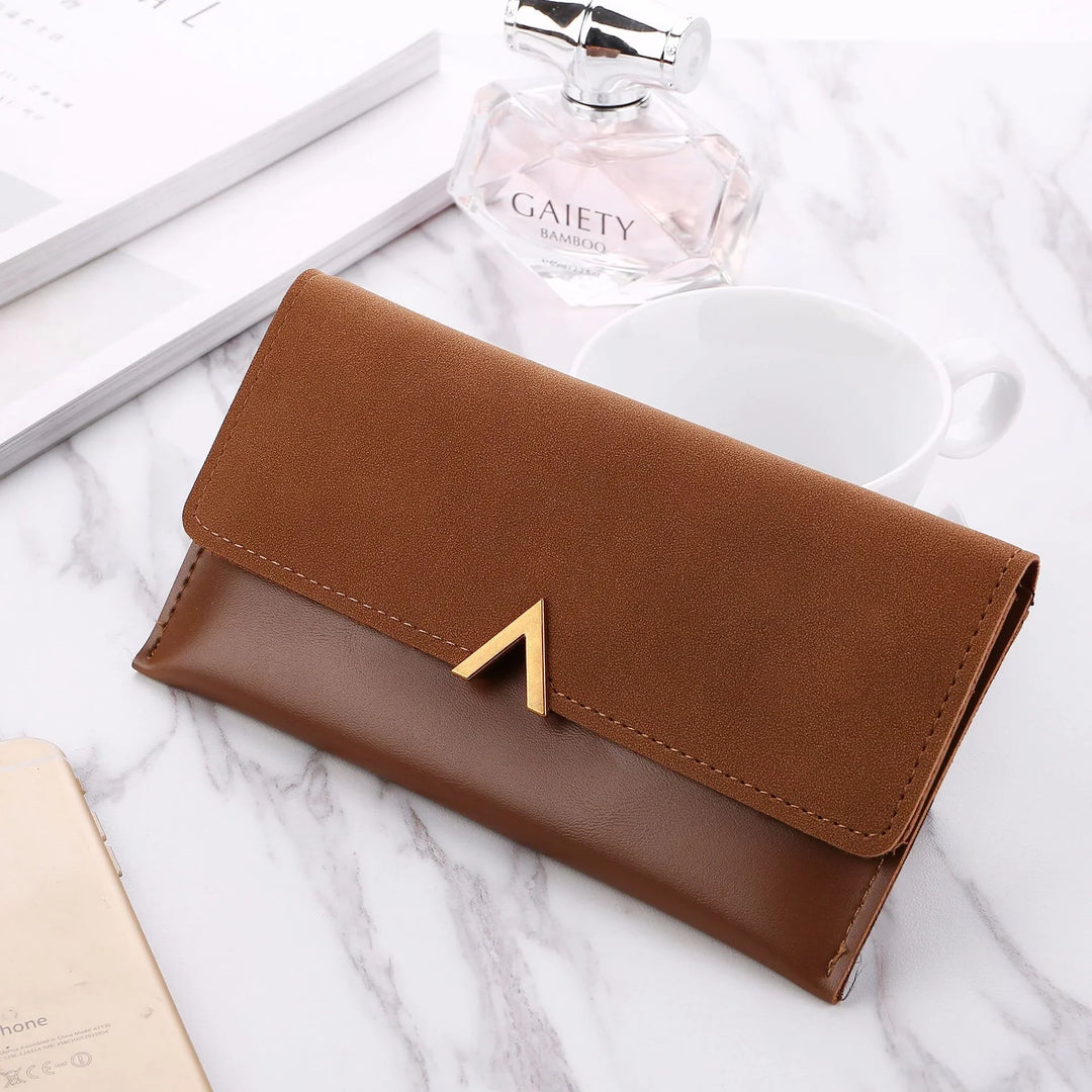 brown leather and suede wallet with gold clasp on marble surface alongside perfume bottle, white cup, and phone