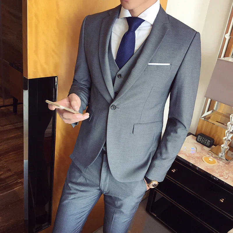 Man wearing grey three-piece suit and navy tie, holding smartphone in modern office setting