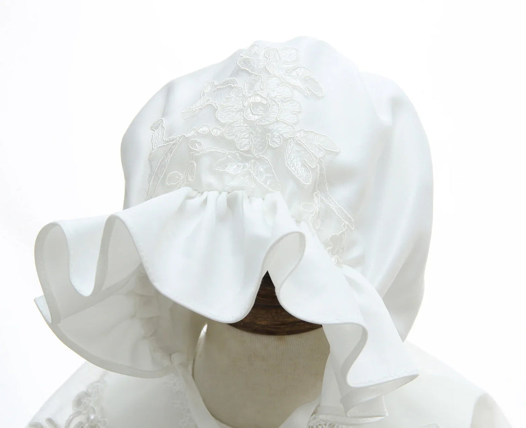 White satin bonnet with floral embroidery and ruffled edge on mannequin