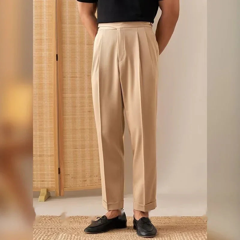 Men's beige pleated dress pants paired with black loafers and a black shirt in a neutral room
