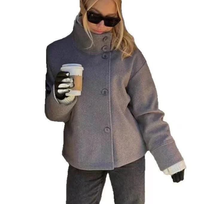 Woman wearing oversized gray button-up coat, black sunglasses, gloves, holding takeaway coffee cup