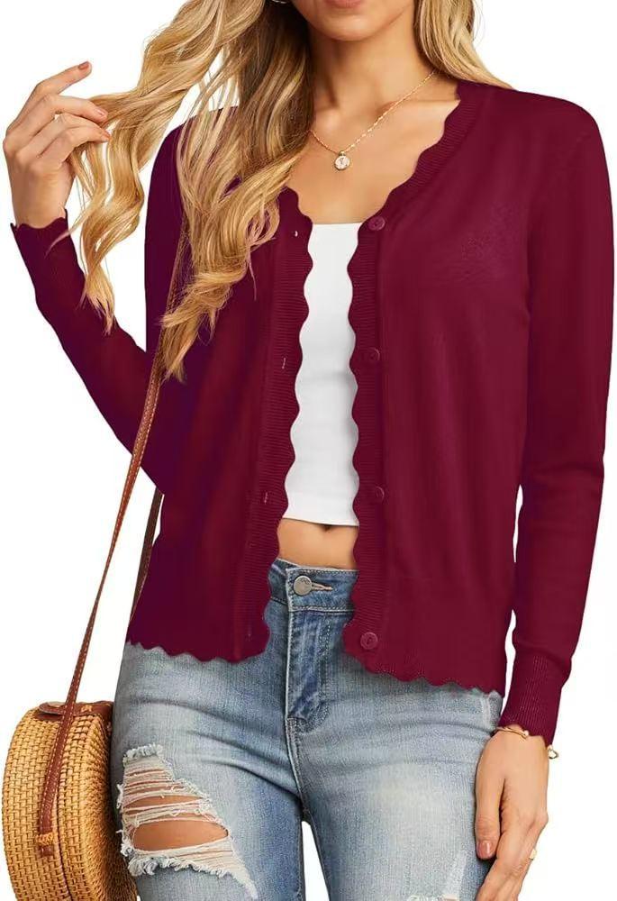 Woman wearing burgundy scalloped button cardigan, white crop top, ripped jeans, and carrying woven bag
