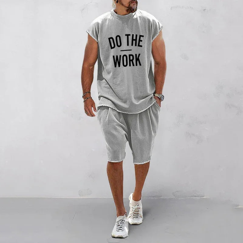 Man wearing gray sleeveless shirt with 'DO THE WORK' text and matching gray shorts and sneakers