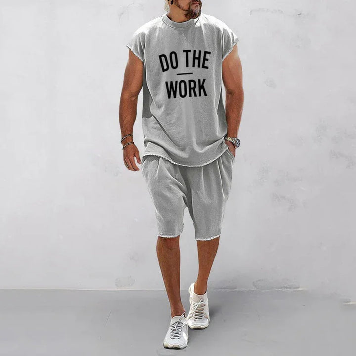 Man wearing gray sleeveless shirt with 'DO THE WORK' text and matching gray shorts and sneakers