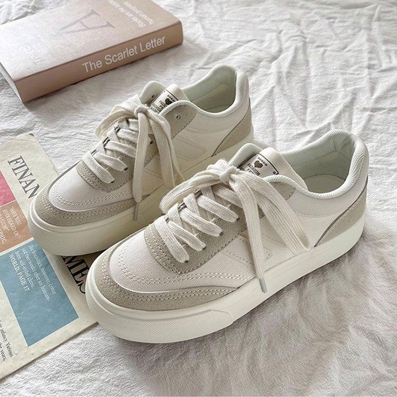 pair of white and beige casual sneakers on white fabric with a book and newspaper nearby