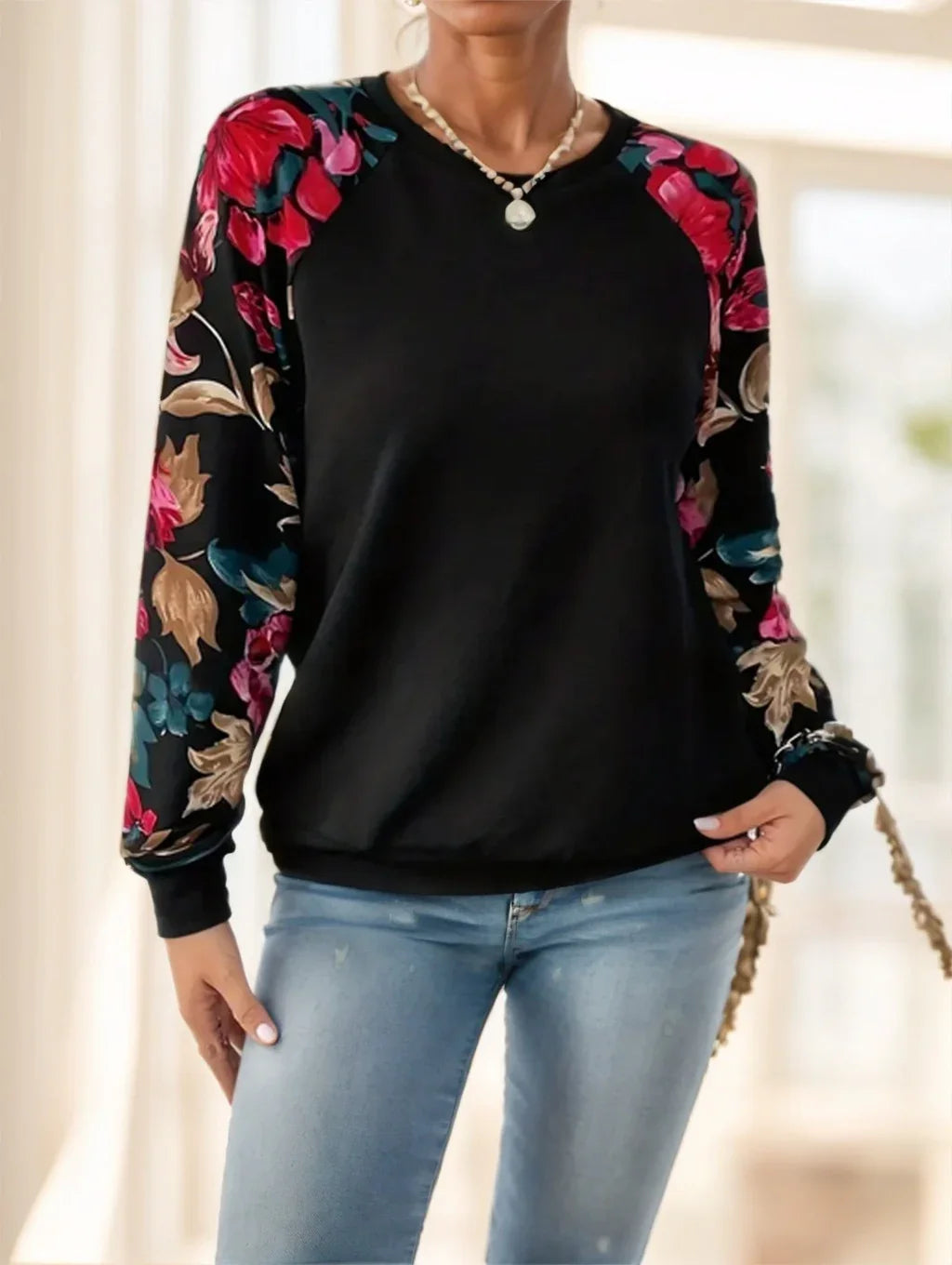 Woman wearing black sweatshirt with floral patterned sleeves and light blue jeans in bright indoor setting