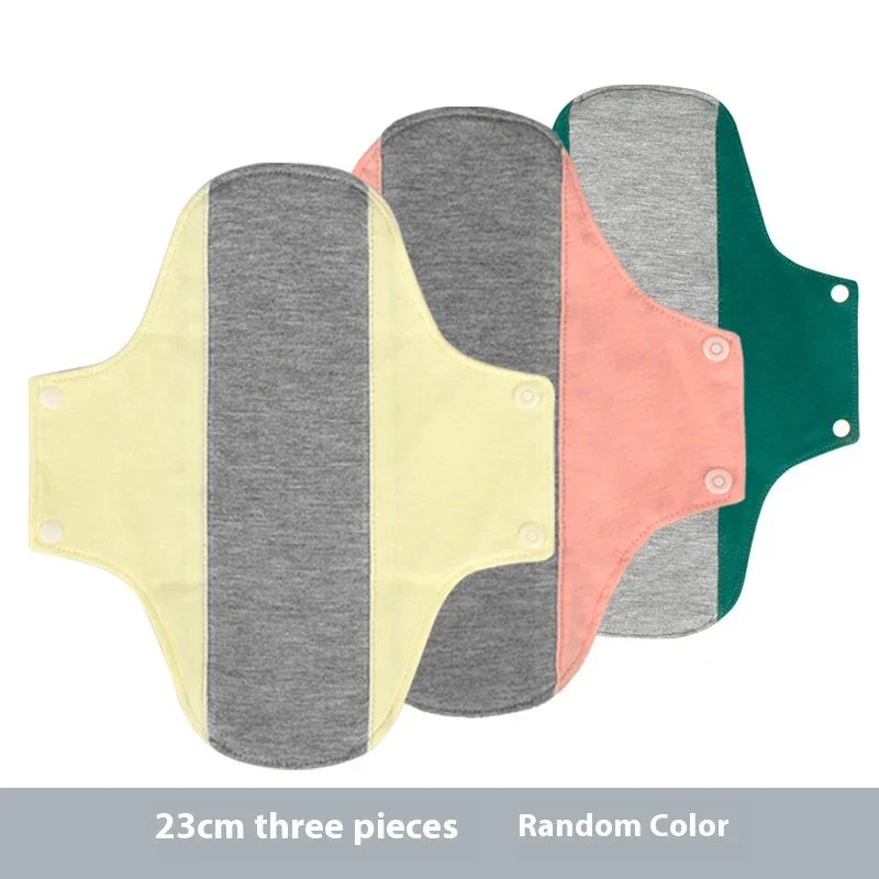 Set of three reusable cloth menstrual pads in yellow, pink, and green with gray center panels