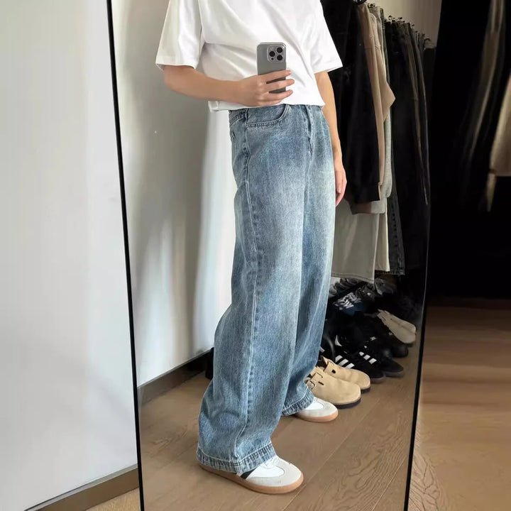 Person in white t-shirt and loose blue jeans taking mirror selfie in wardrobe with shoes and clothes