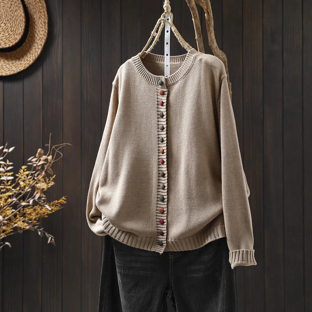 Beige knit cardigan with colorful buttons hanging on rustic wooden hanger against dark wood wall