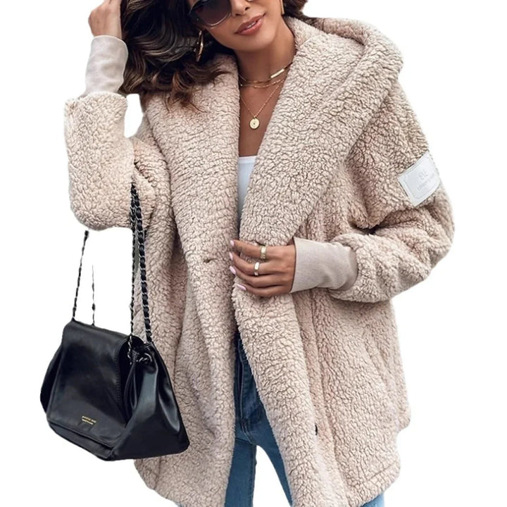Woman wearing beige sherpa fleece jacket with ribbed cuffs, blue jeans, sunglasses, and carrying black leather handbag