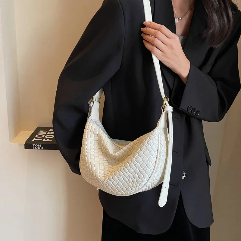 Woman wearing black blazer holding a white woven leather shoulder bag indoors