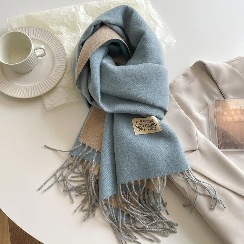 Soft blue and beige scarf with fringe on white table next to cream blazer and coffee cup