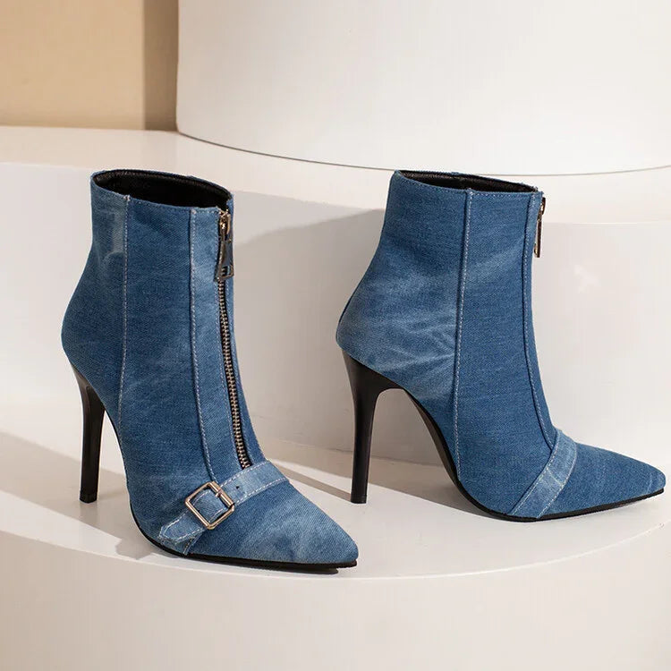 Blue denim high-heeled ankle boots with front zipper and buckle detail on white curved surface
