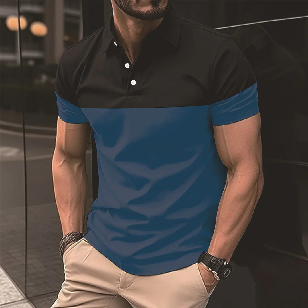 Man wearing black and blue color block polo shirt with beige pants standing against dark reflective wall