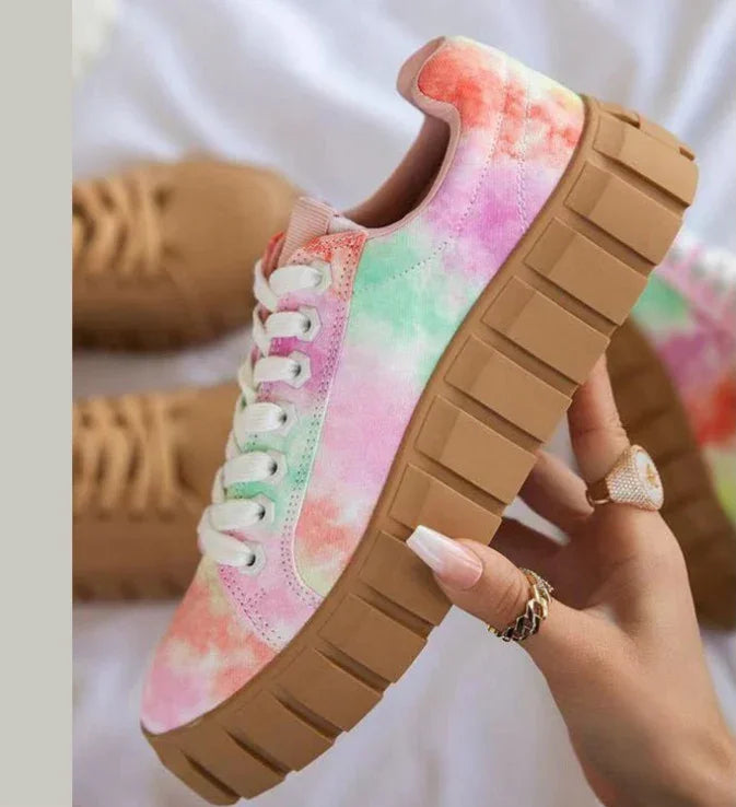 Hand holding colorful tie-dye platform sneaker with thick brown sole and white laces